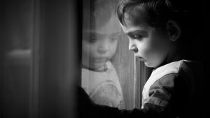 niño pequeño triste mirando por la ventana